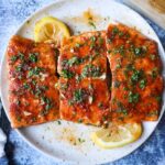 plate with 3 salmon filets topped with parsley, cajun seasoning, and honey butter sauce, side of lemon