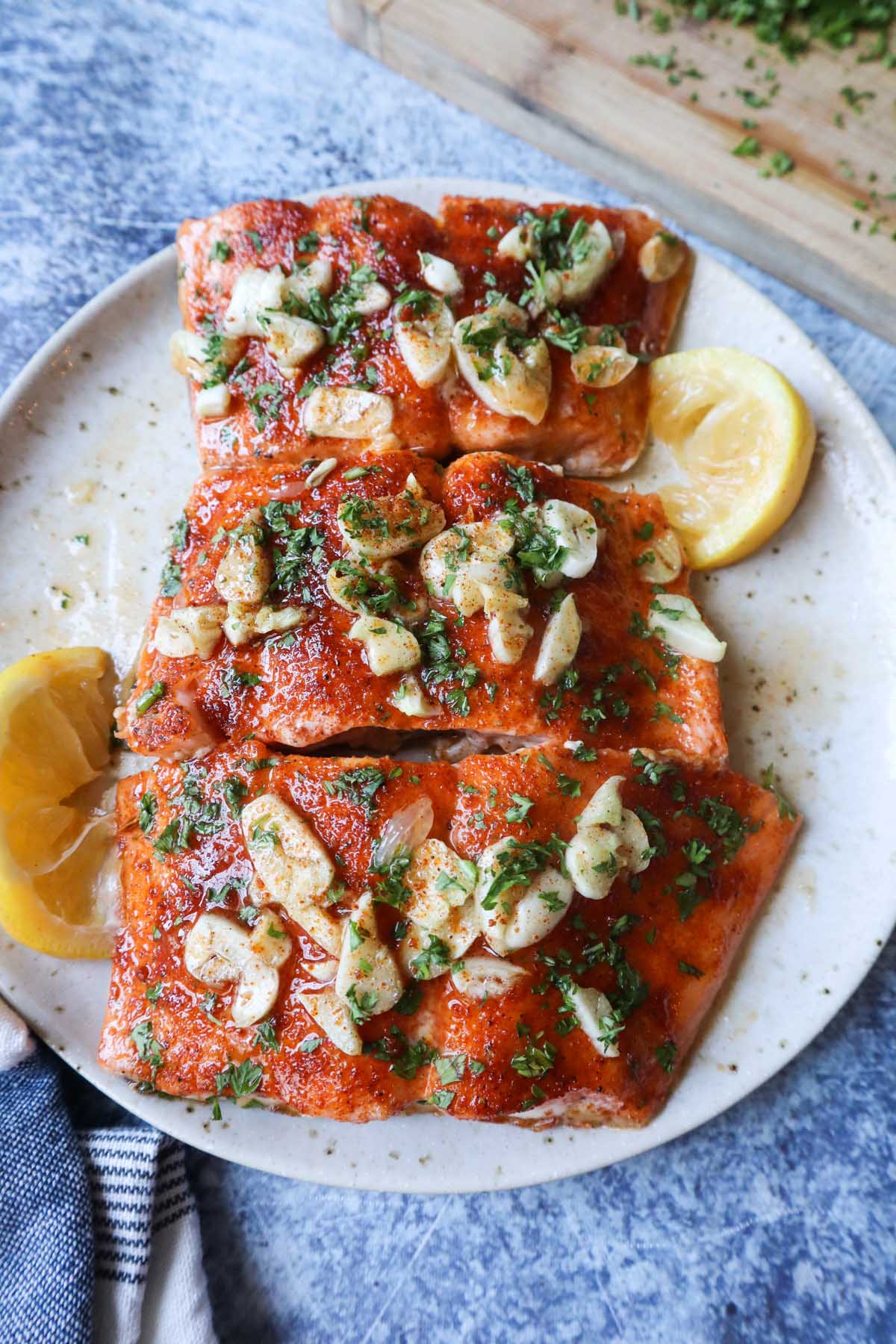 white plate with cooked cajun salmon topped with garlic parsley and honey butter sauce