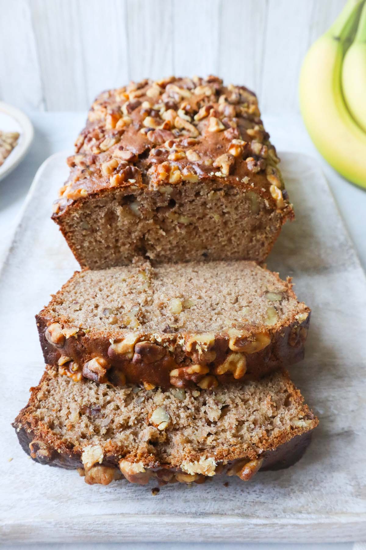 4 ingredient banana bread topped with walnuts with two slices cut off of the loaf and a banana in the background