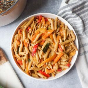 white bowl with creamy vegan rasta pasta topped with orange and red bell peppers with green onion
