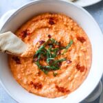 white bowl with paprika dip topped with fresh basil and paprika with pita chip sticking out