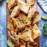 wooden cutting board with carne asada quesadillas surrounded by cilantro and lime slices