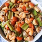 close up of shrimp chop suey in a white bowl with a blue background