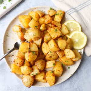 air fryer lemon greek potatoes on a white plate with two slices of lemon