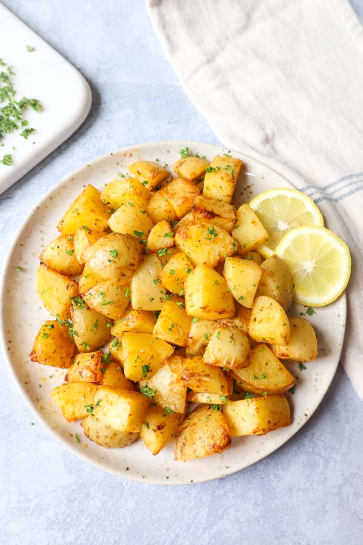 air fryer lemon greek potatoes on a white plate with two slices of lemon