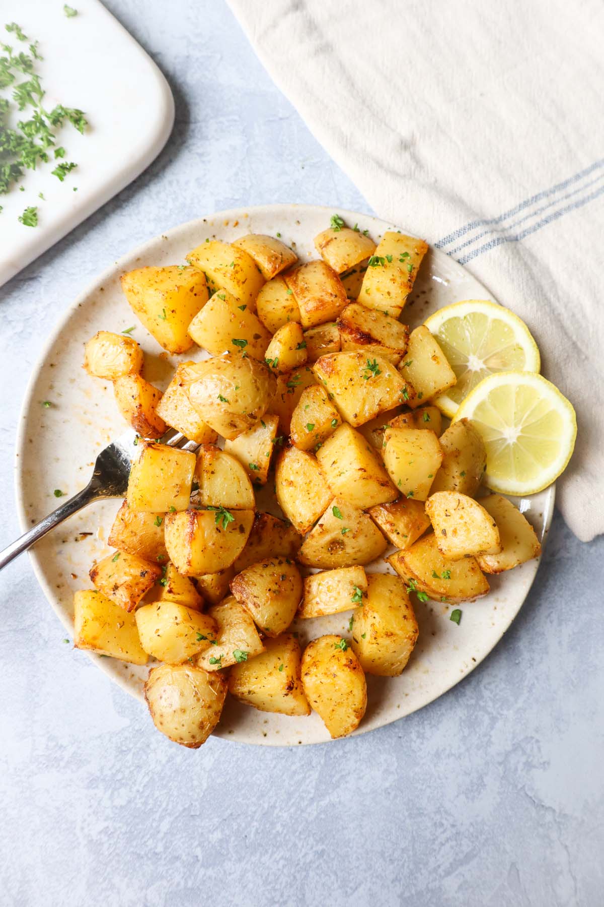 air fryer lemon greek potatoes on a white plate with two slices of lemon and a fork
