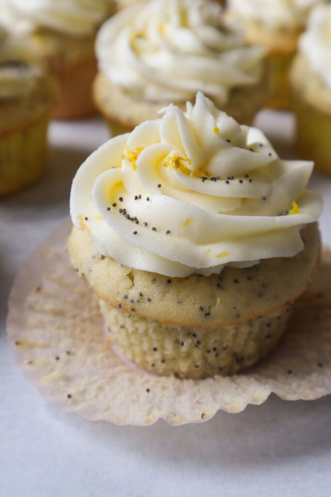 one cupcake topped with lemon buttercream icing, lemon zest, and poppyseeds
