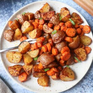 white plate with air fried carrots and potatoes topped with green onion