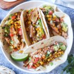 white plate with 4 blackened tacos topped with an avocado pico de gallo and blackened corn