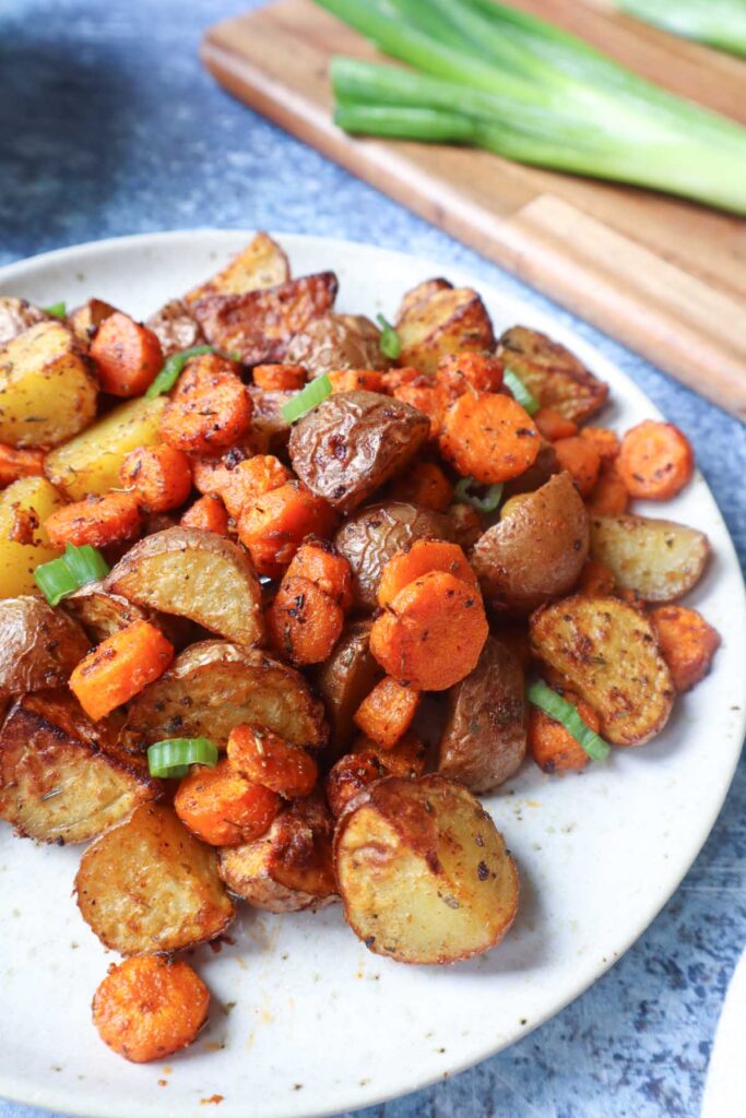 white plate with air fried carrots and potatoes topped with green onion