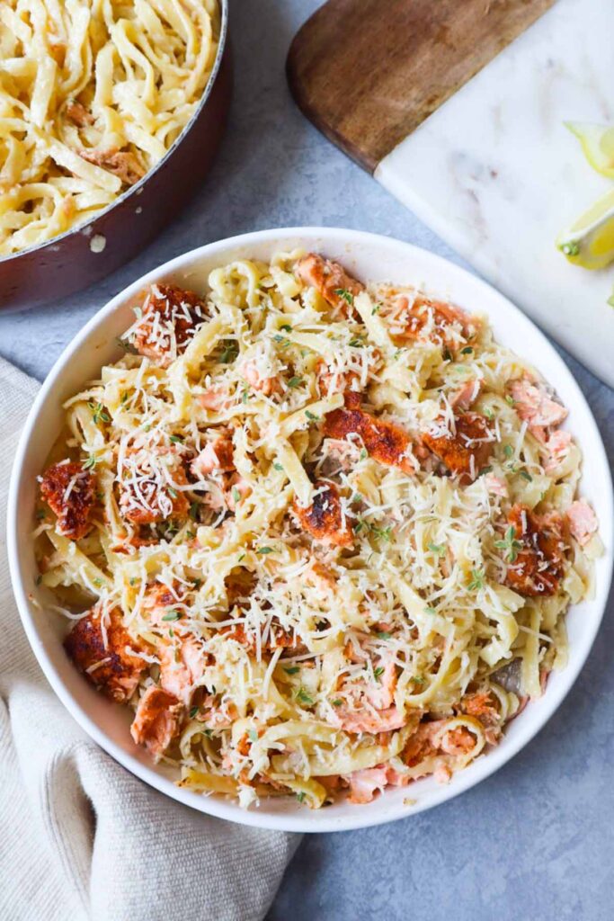 white bowl with fettuccine alfredo topped with parmesan and cajun salmon