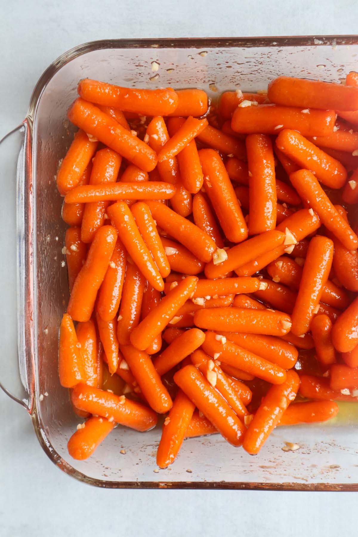glass dish with baby carrots with garlic and the hot honey sauce before they're roasted