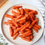 white plate with roasted carrots topped with a hot honey sauce and fresh thyme