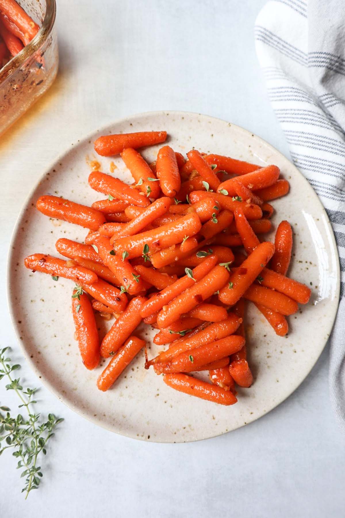 white plate with roasted carrots topped with a hot honey sauce and fresh thyme