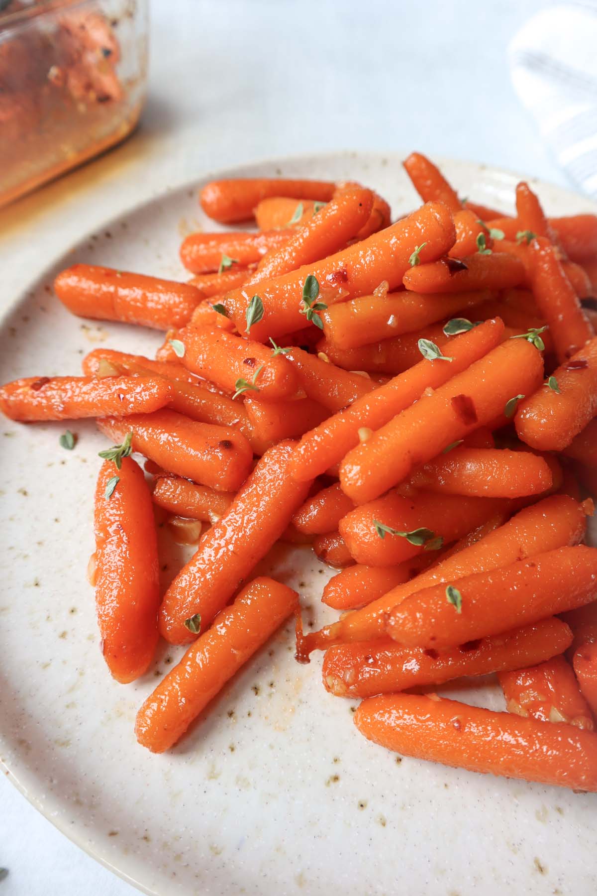 white plate with roasted carrots topped with a hot honey sauce and fresh thyme