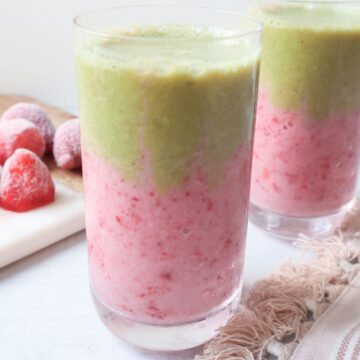 two glasses with strawberry matcha smoothie with a pink strawberry layer at the bottom and a green matcha layer on top