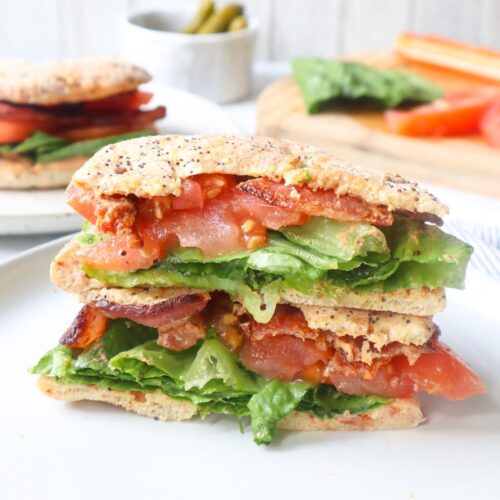 white plate with an everything bagel BLT sandwich sliced in half with the halves stacked on one another
