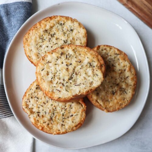 white plate with four slices of french bread topped with cheese, butter, and italian seasoning