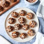 white plate with various biscoff balls topped rolled in crushed biscoff cookies and topped with chocolate drizzle and toasted coconut with chocolate bowl and toasted coconut on a cutting board