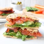 white plate with an everything bagel BLT sandwich sliced in half with the halves stacked on one another
