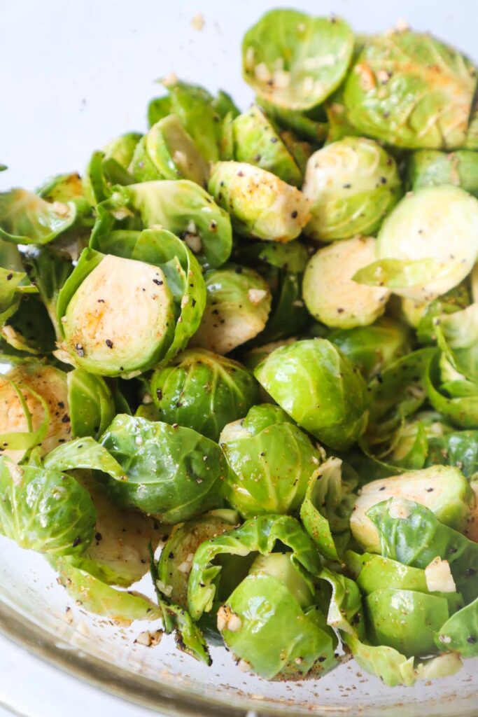 clear bowl with seasoned brussel sprouts before they're baked