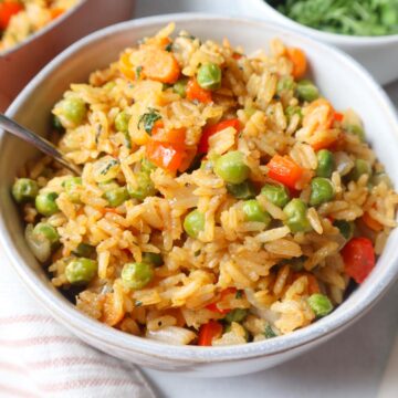 green curry fried rice in a white bowl with carrots, peas, and pepper, topped with fresh cilantro