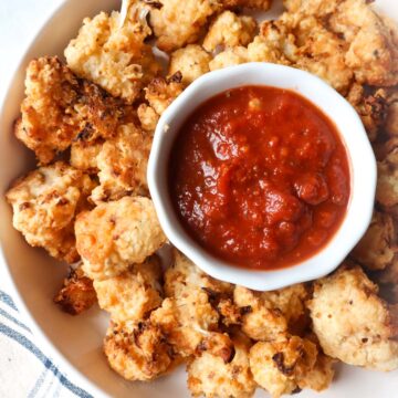 white bowl with air fryer cauliflower parmesan with warmed marinara in a cup