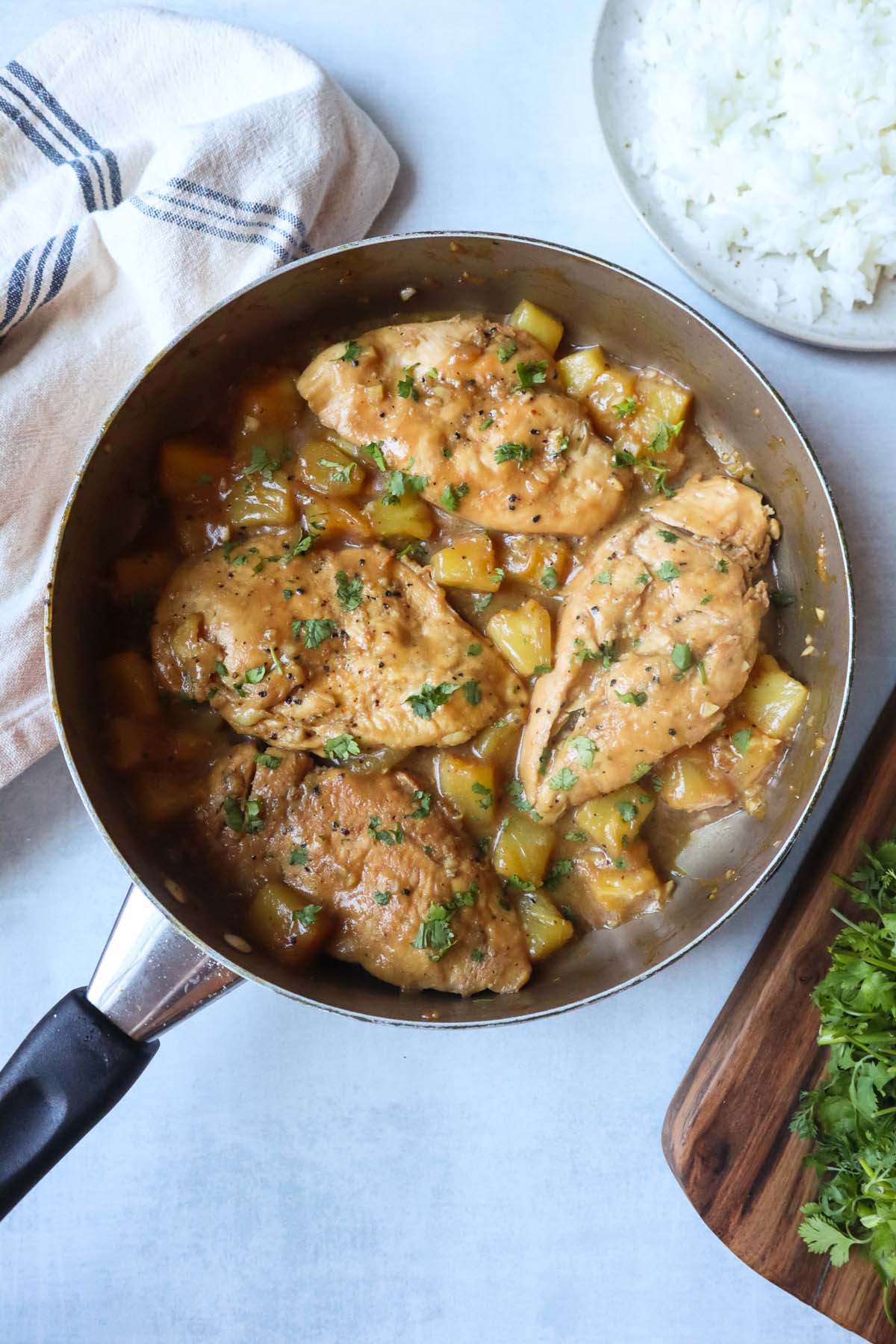 skillet with chicken and pineapples in a sauce topped with fresh herbs