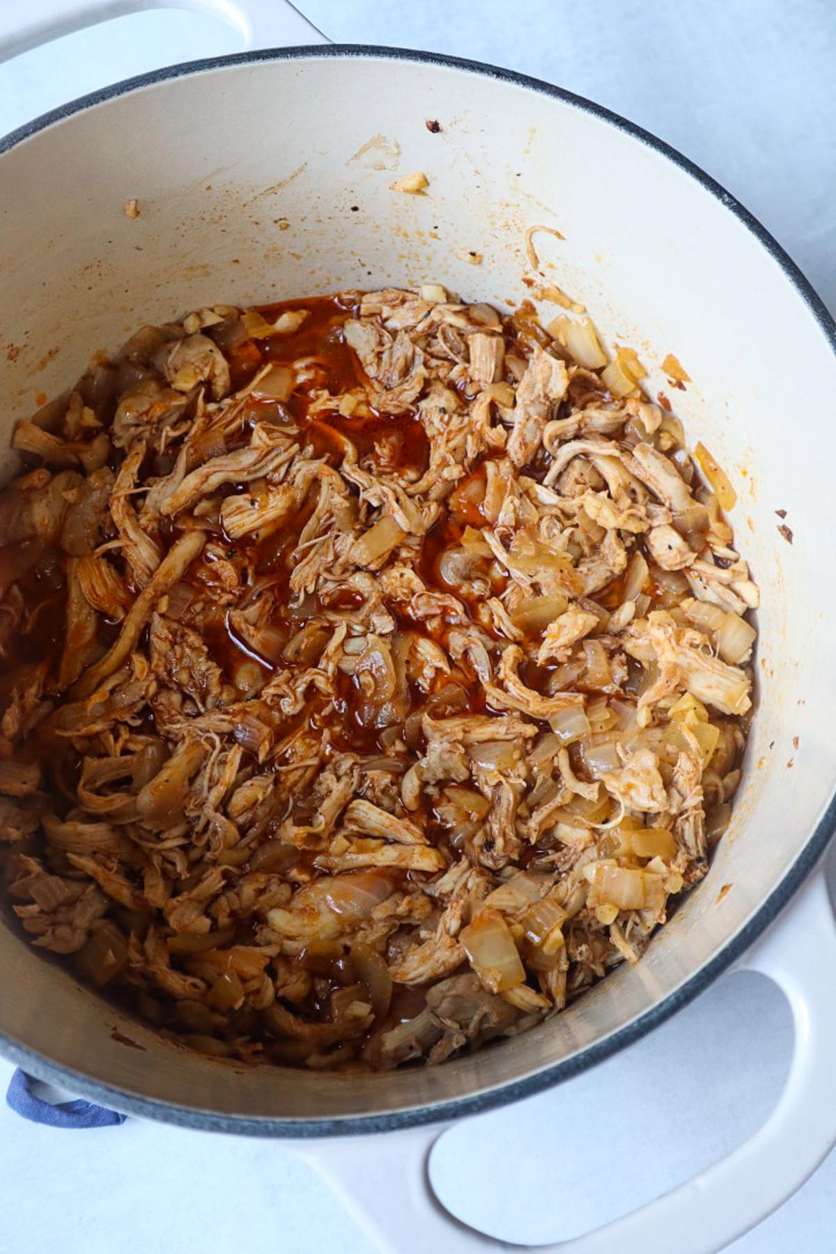 dutch oven with shredded cooked chicken with onion in a savory broth