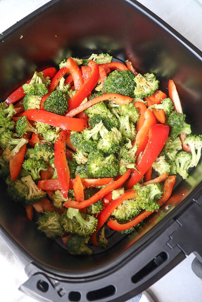 air fryer basket with seasoned red bell pepper and broccoli