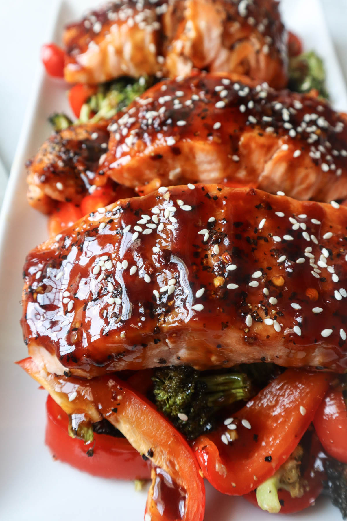 white plate with red bell pepper, broccoli, cooked salmon topped with sauce and sesame seeds