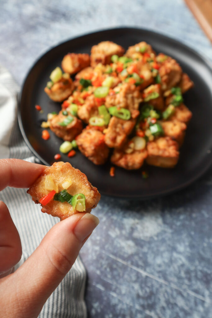 hand holding air fryer salt and pepper tofu topepd with green onion, thai chili, and garlic