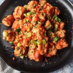 black plate with salt and pepper tofu topped with green onion, red chili pepper, and garlic