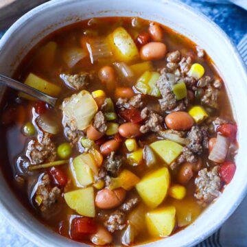 white bowl with spoon with cowboy soup with potatoes, beef, and beans