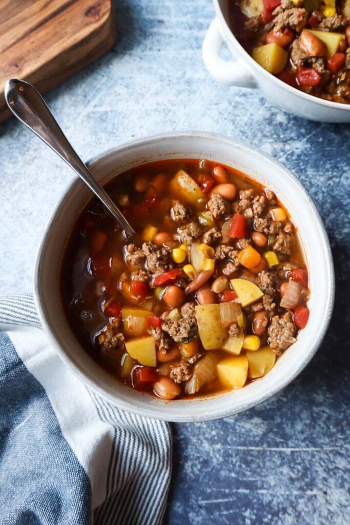 white bowl with spoon with cowboy soup with potatoes, beef, and beans