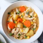 white bowl with chicken soup with vegetables, chicken, and parsley