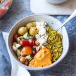 white bowl with quinoa, feta, olives, hummus, and tomato cucumber salad