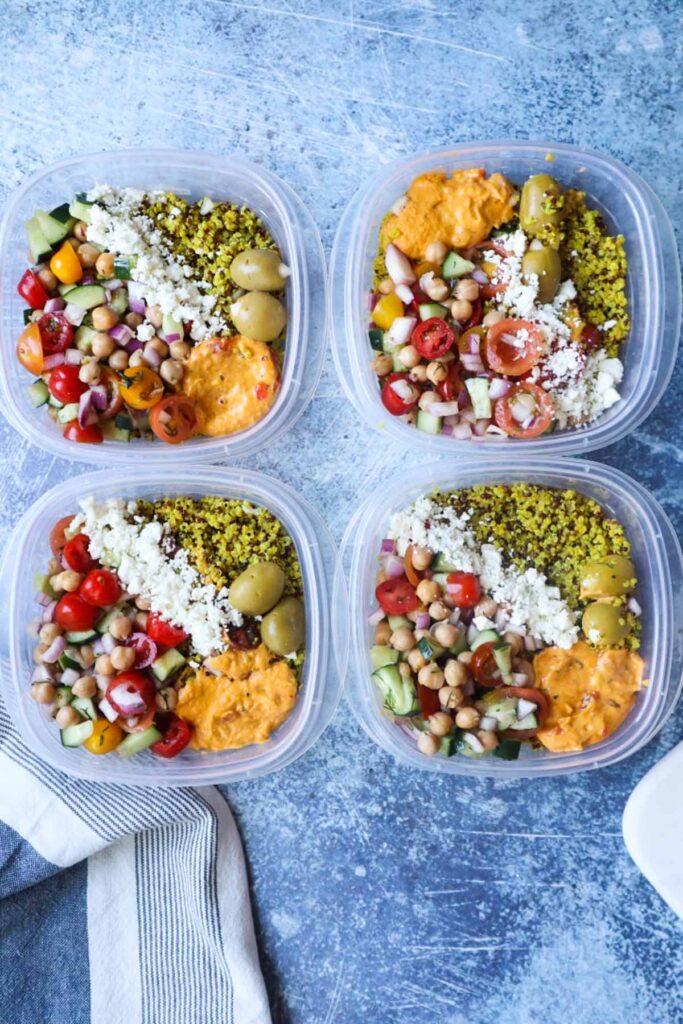 clear plastic containers with mediterranean power bowls with quinoa, feta, olives, hummus, and tomato cucumber salad