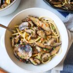 white bowl with spaghetti and mushrooms topped with red pepper flake and fresh thyme