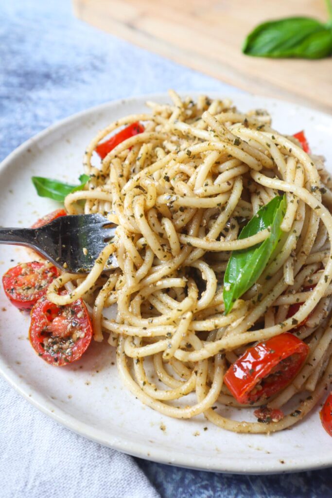 white plate with spaghetti, pesto, grape tomatoes, and two slices of basil