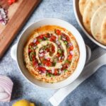 beiruti hummus in a white bowl topped with parsley, red pepper, and red onion