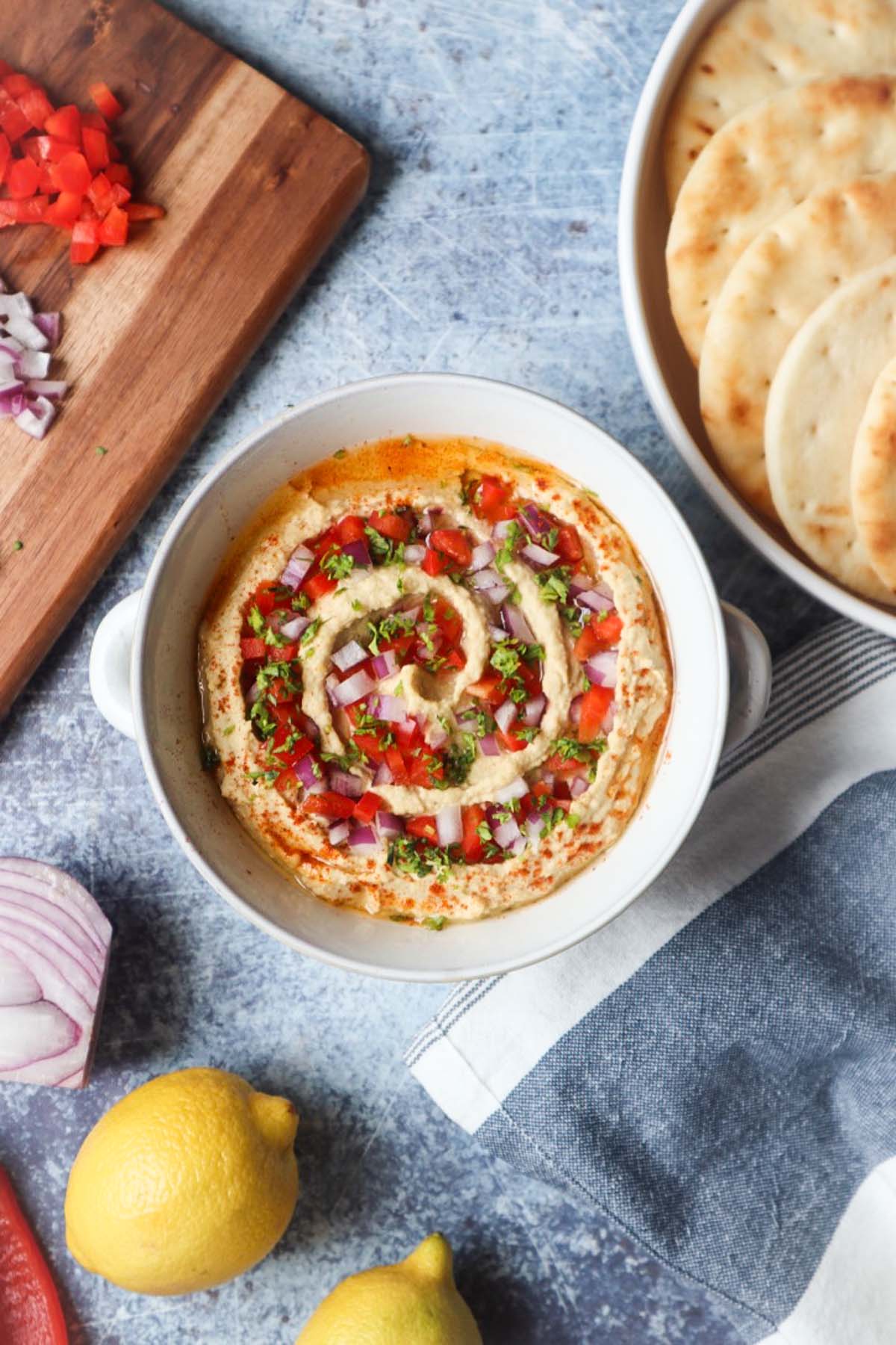 beiruti hummus in a white bowl topped with parsley, red pepper, and red onion