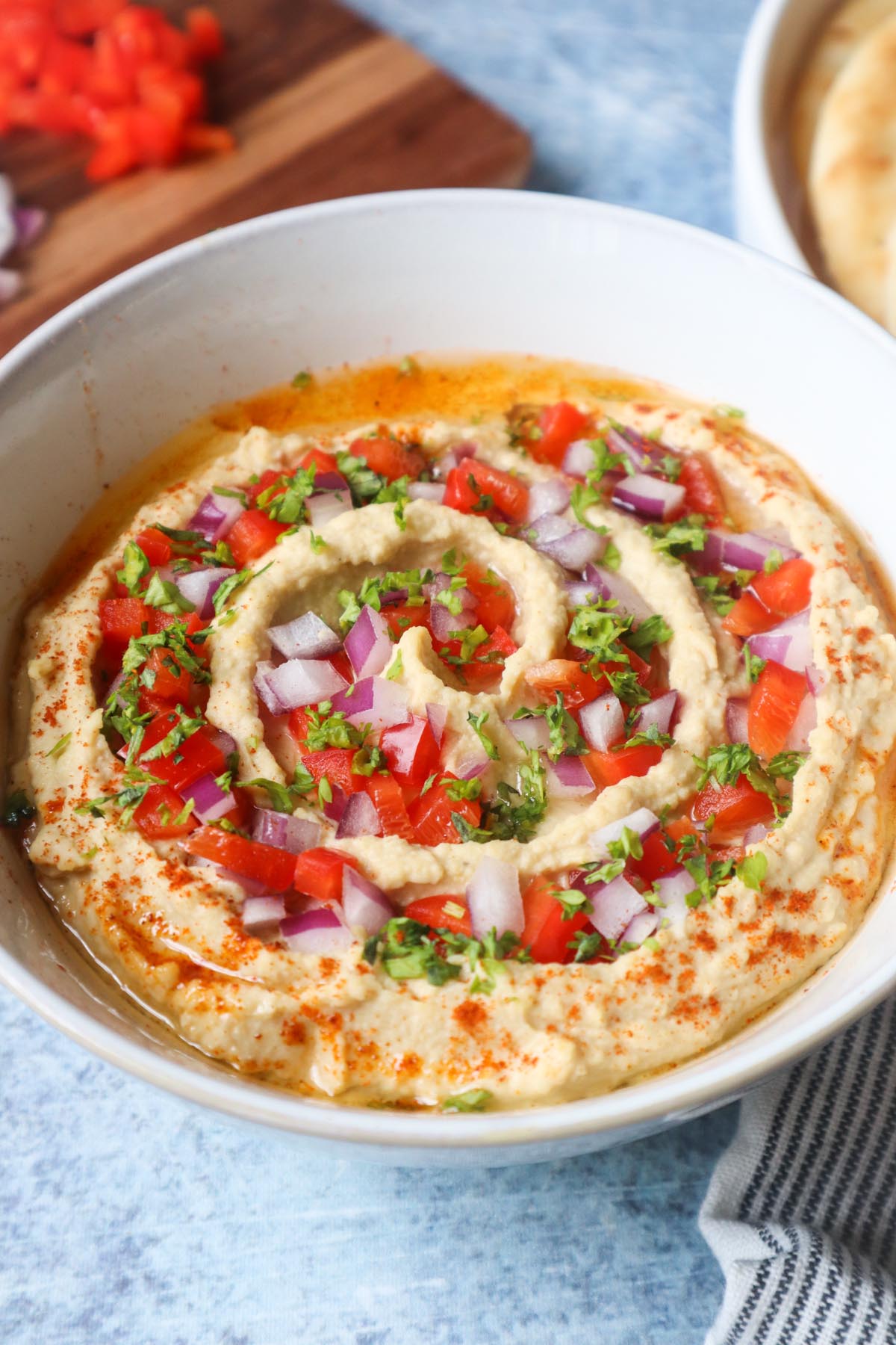 beiruti hummus in a white bowl topped with parsley, red pepper, and red onion