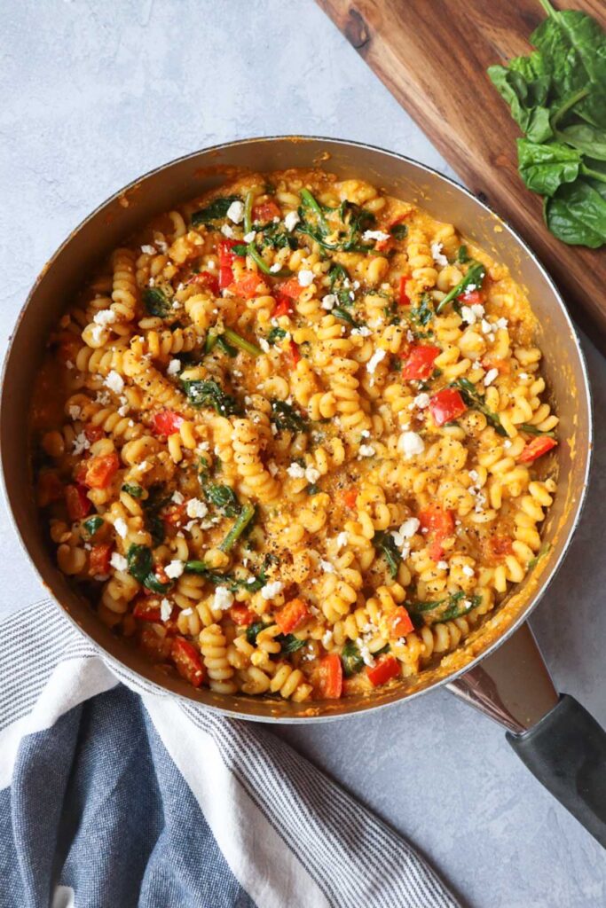 skillet with pumpkin feta pasta topped with feta cheese, red bell pepper, and spinach