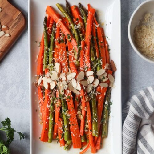 white plate with carrots and asparagus topped with cheese and sliced almonds