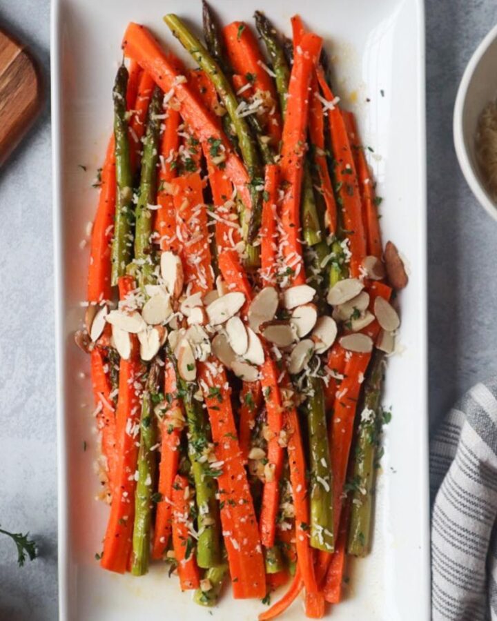 white plate with carrots and asparagus topped with cheese and sliced almonds