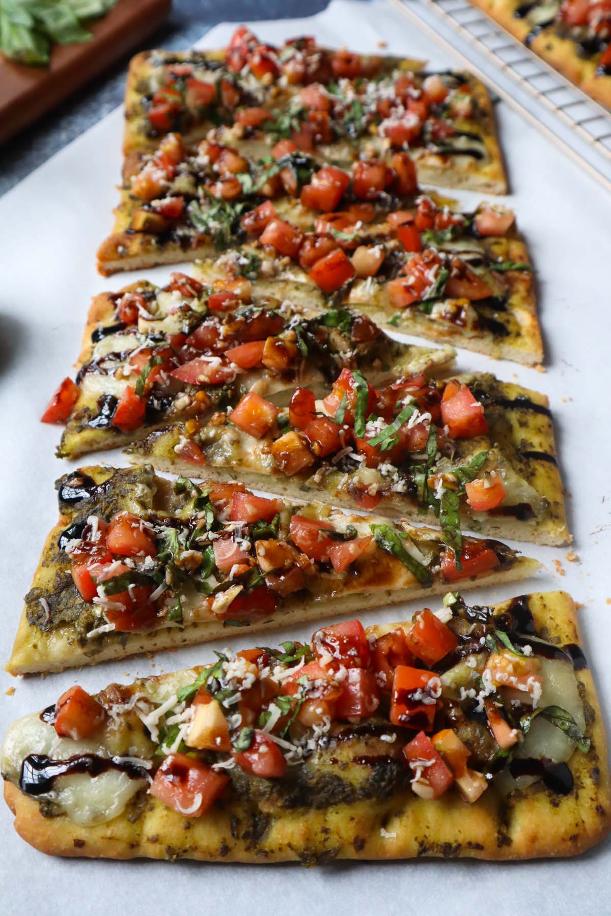 parchment paper with flatbread topped with bruschetta, cheese, and balsamic glaze