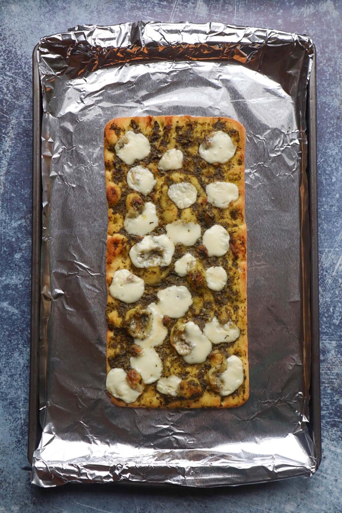 baking pan covered in foil with flatbread topped with pesto and mozzarella