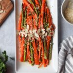 white plate with carrots and asparagus topped with cheese and sliced almonds
