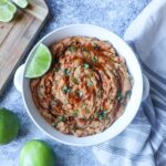 white bowl with chipotle refried beans topped with fresh cilantro, lime, and adobo.